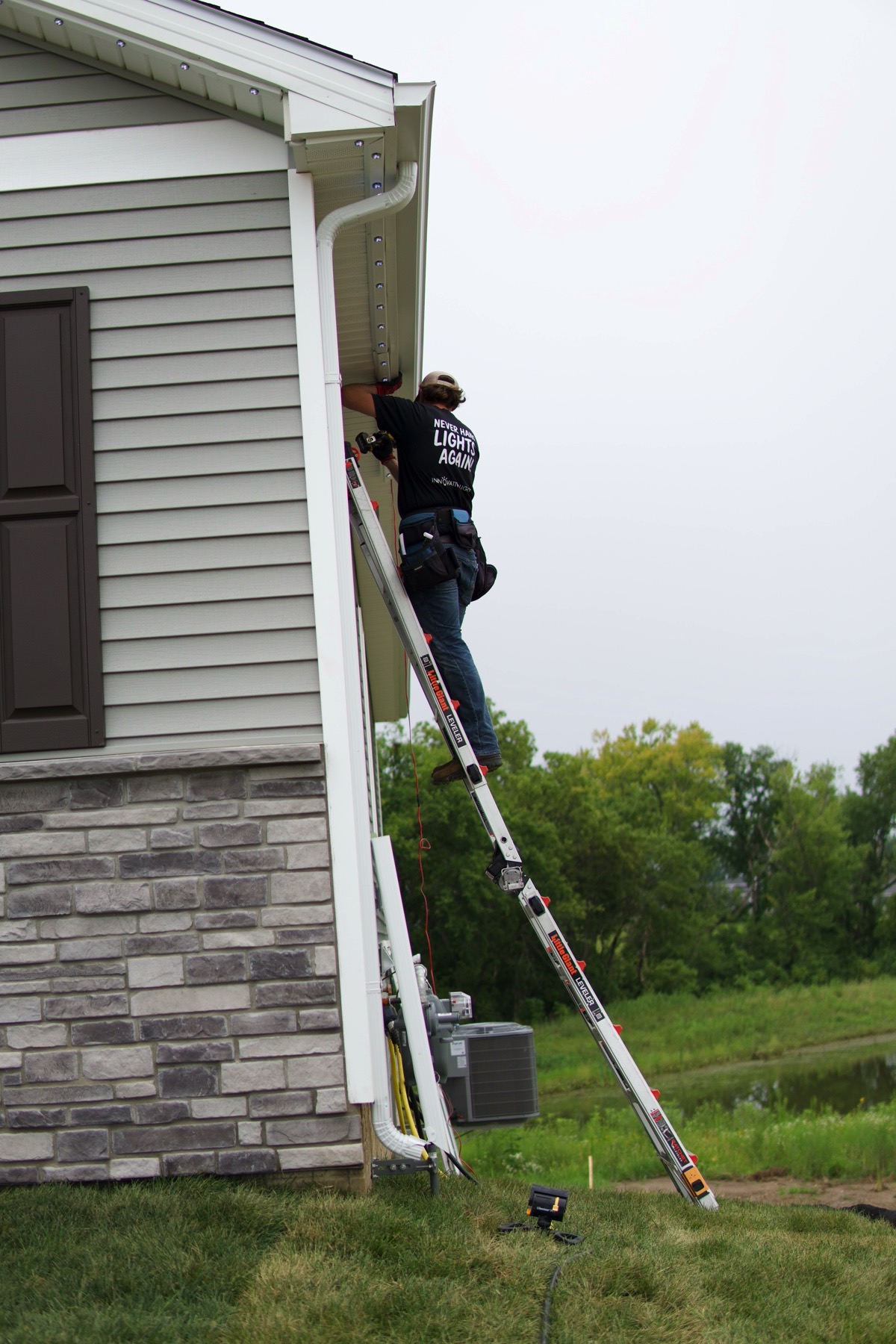 Installer on a ladder fitting permanent lighting under a roofline